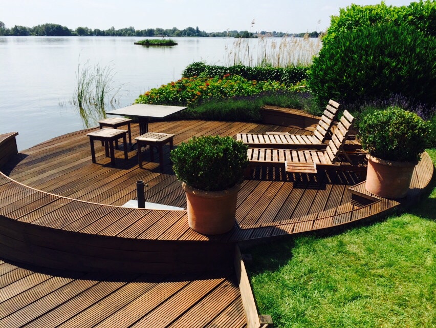 Voordelen van vlonder oliën: bescherming, kleurbehoud en luxe uitstraling Geoliede houten vlonder aan het water met tuinmeubels, mooi beschermd tegen vergrijzing en weersinvloeden